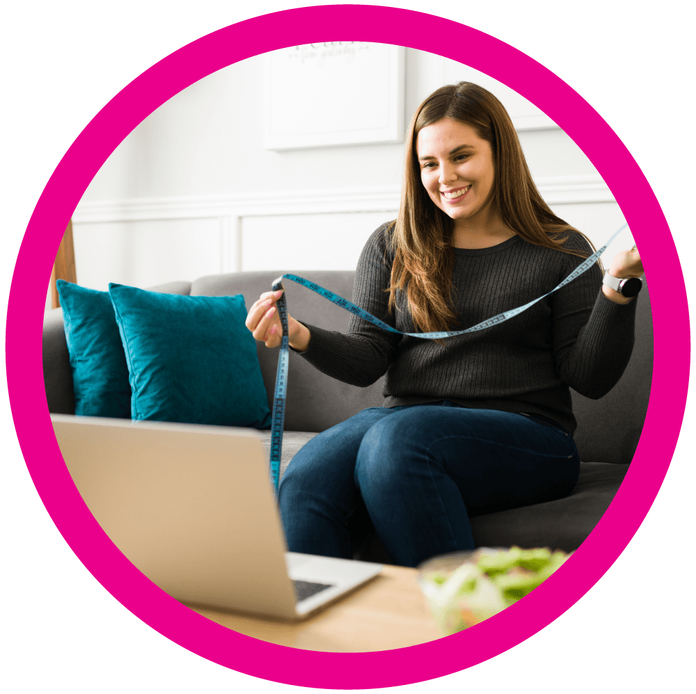 A woman sitting on a sofa holds a tape measure in front of a laptop after telemedicine weight loss